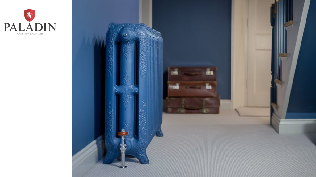 A blue cast iron radiator stands in a carpeted room with blue walls, near a staircase and a stack of vintage suitcases; Paladin logo is visible on the left.